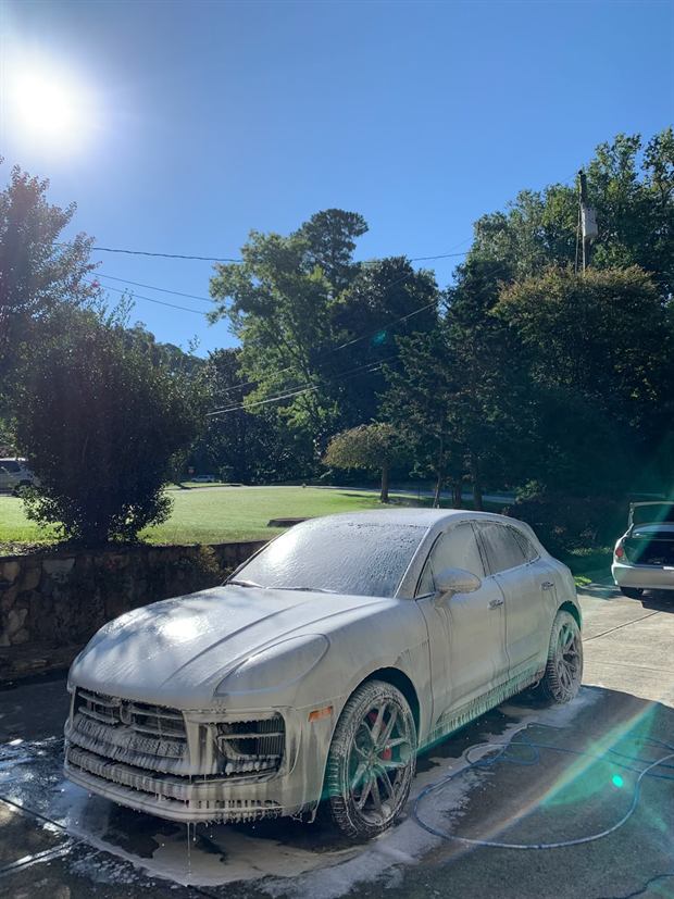 A Porsche Macan covered in foam on a sunny driveway