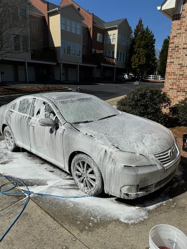 A sedan under a full foam bath beside a house